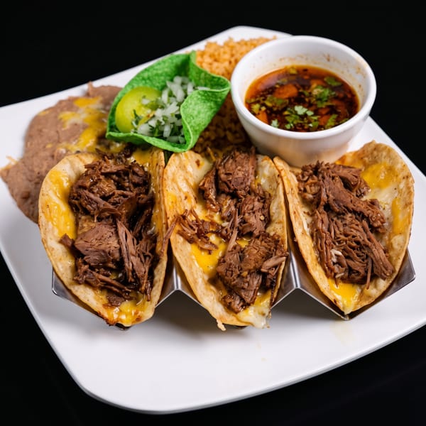 Three birria tacos with melted cheese and shredded beef, served with rice, refried beans, and consommé.