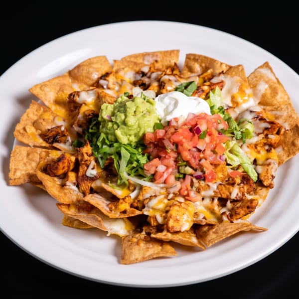 Chicken nachos with melted cheese, guacamole, sour cream, pico de gallo, and lettuce on a white plate.